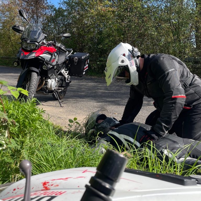 Realistische Simulationen Ein Motorradfahrer liegt verletzt im Straßengraben. Ein anderer kniet über ihm und versorgt ihn